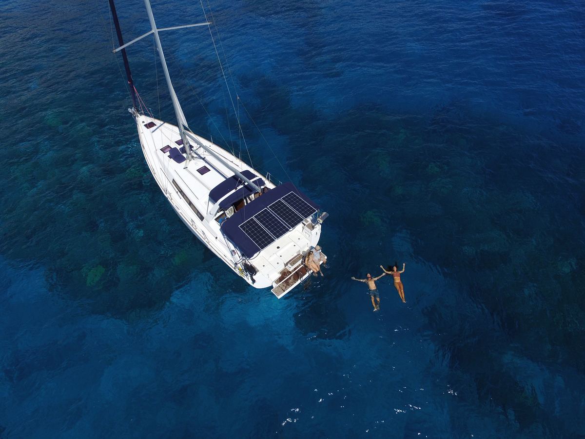 Aerial view of SV Kainani at anchor above the reef, two swimmers off the stern