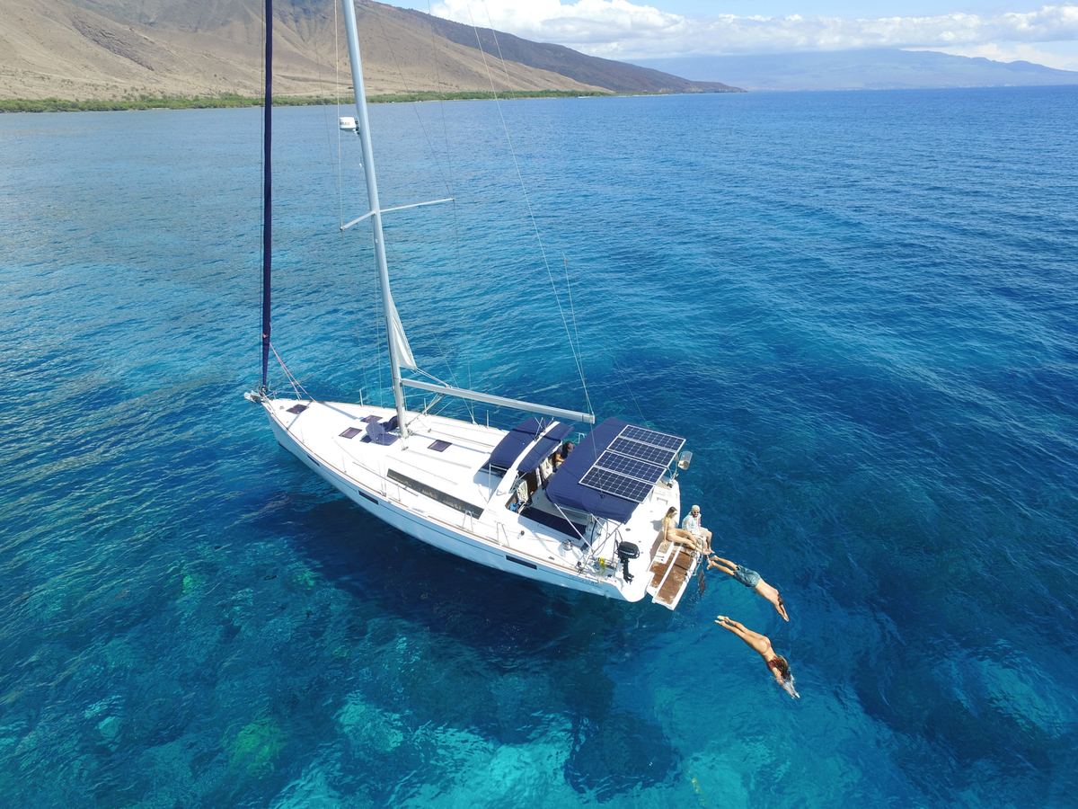 Aerial view of SV Kainani at anchor over a clear reef as guests swim from the stern