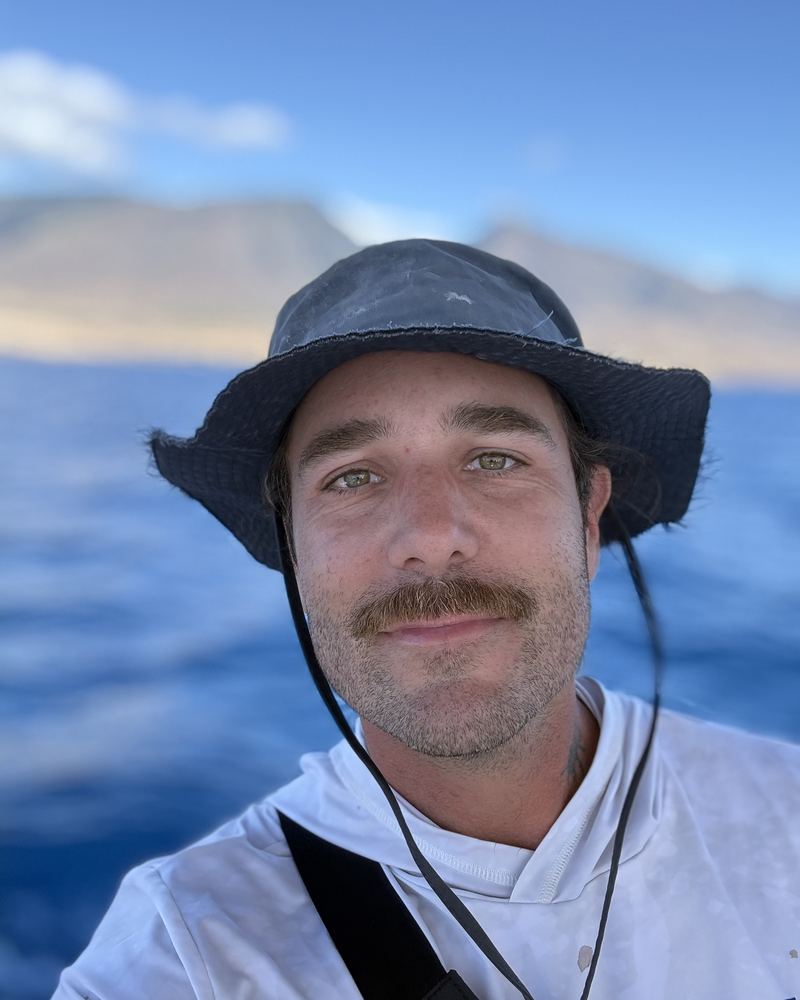 Captain Noah in a bucket hat on the water, the West Maui Mountains behind