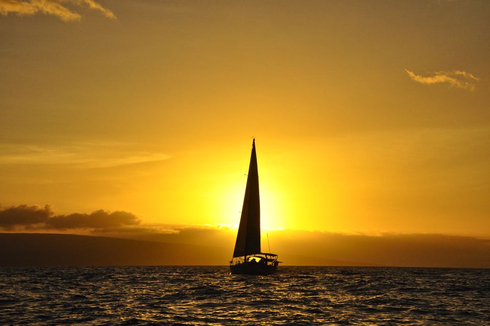 A sailboat silhouetted against a golden West Maui sunset